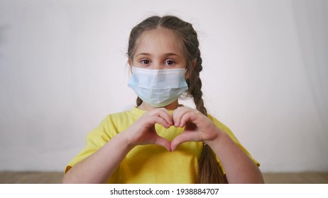 face child protective mask shows a gesture heart. stay home coronavirus quarantine kid dream concept. little girl wearing a medical protective mask. kid child shows heart gesture protection - Powered by Shutterstock