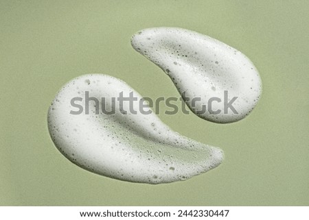 Face cleansing mousse drops sample. White cleanser or soap foam bubbles on green background. Cleanser gel, hair shampoo foam texture closeup.