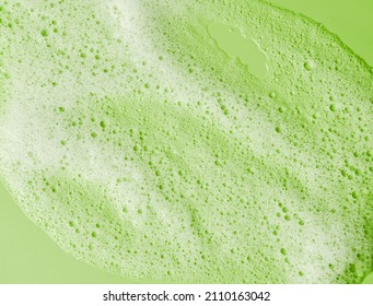 Face Cleansing Mousse Sample. White Cleanser Foam Bubbles On Green Background. Soap, Shower Gel, Shampoo Foam Texture Closeup.