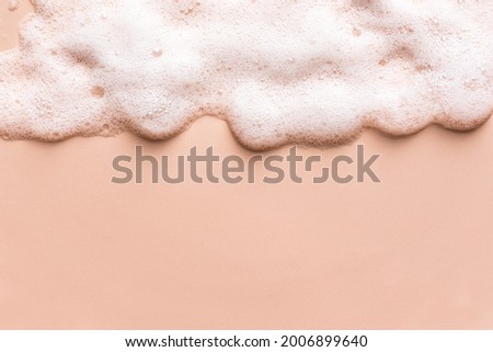 Face cleansing mousse sample. White cleanser foam bubbles on nude background, copy space. Soap, shower gel, shampoo foam texture border.