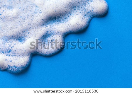 Face cleansing mousse sample. White cleanser foam bubbles on blue background, copy space. Soap, shower gel, shampoo foam texture closeup.