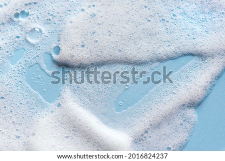 Face cleansing mousse sample. White cleanser foam bubbles on blue background. Soap, shower gel, shampoo foam texture closeup.