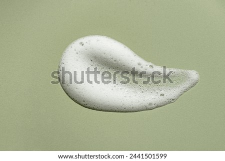 Face cleansing mousse sample. White cleanser or soap foam bubbles on olive green background. Shower gel, hair shampoo foam texture closeup.