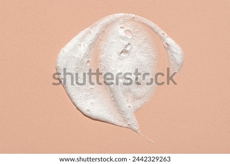 Face cleansing mousse sample. White cleanser foam bubbles on pink beige background. Soap, shower gel, shampoo foam texture closeup.