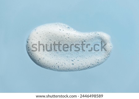 Face cleansing mousse sample. White cleanser or soap foam bubbles on blue background. Shower gel, bubble mask, shampoo foam texture closeup.