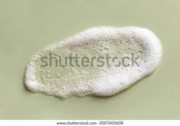 Face cleansing mousse sample. White cleanser\
foam bubbles on green background. Soap, shower gel, shampoo foam\
texture closeup.