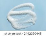 Face cleansing mousse smudge sample. White cleanser or soap foam bubbles on blue background. Shower gel, hair shampoo foam smear texture.