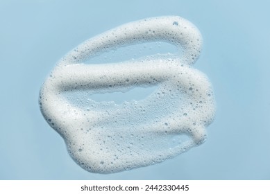 Face cleansing mousse smudge sample. White cleanser or soap foam bubbles on blue background. Shower gel, hair shampoo foam smear texture.