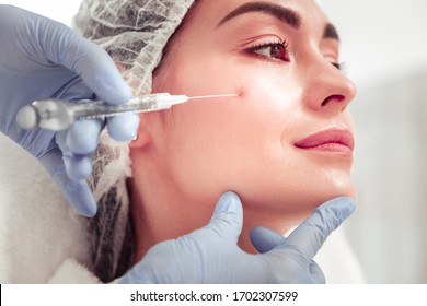 Face of client. Cosmetologist wearing gloves touching face of client doing beauty shot - Shutterstock ID 1702307599