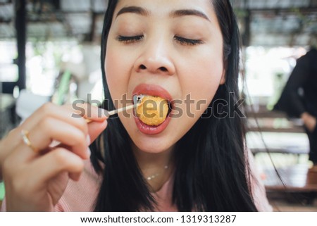Face close up of Asian woman eat cheese balls with sticks.