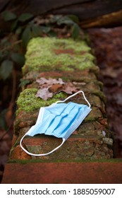 Face Covering Mask Dropped As Litter On A Broken Wall In Winter Leaves - PPE Mask Used Once - Close Up