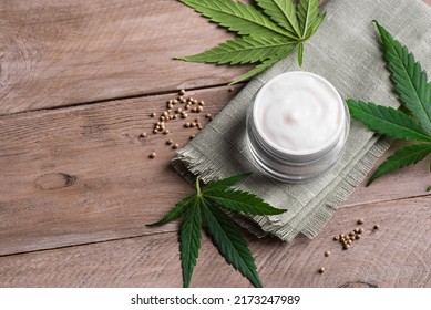 Face Cream And Hemp Plant Green Leaves On Wooden Background, Copy Space. Alternative Medicine, Cbd Oil And Organic Skin Care Concept.