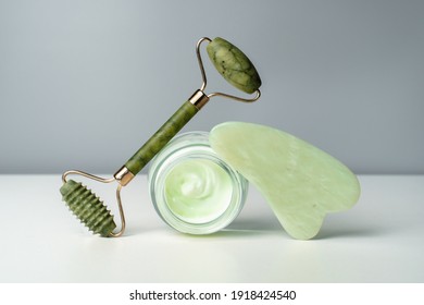 Face cream and jade massage roller. Lifting for healthy and youthful skin. Organic cosmetics on a black background. 
Trending skin care. Gouache scraper for face and neck massage