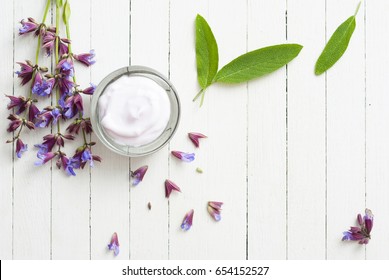 face cream with sage herbal flowers on white wooden table background