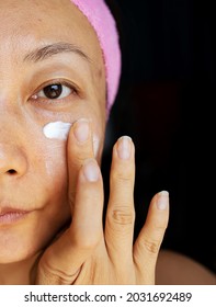 Face Cream Woman Applying Cream To The Skin Under The Eyes. Beauty Eye Contour Wrinkle Cream Or Anti-aging Skin Care Cream. Beautiful Young Mixed Race Asian Caucasian Beauty Model Isolated On Black