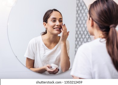 Face cream. Young beautiful woman wearing white shirt putting face cream on her nice healthy skin