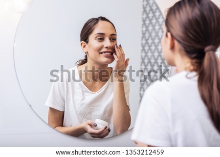 Face cream. Young beautiful woman wearing white shirt putting face cream on her nice healthy skin