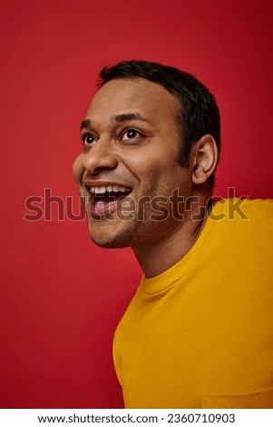 face expression, amazed indian man in yellow t-shirt laughing on red background, open mouth