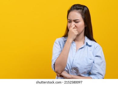 Face expression of human.  Asian female smelling disgusted odor and pinching his nose in studio shoot yellow background.