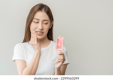 Face expression suffering from sensitive teeth and cold, asian young woman, girl hand touching her cheek, feeling hurt, pain eating ice cream, lolly. Toothache molar tooth at home, dental problem.