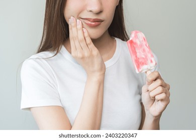 Face expression suffering from sensitive teeth and cold, asian young woman, girl hand touching her cheek, feeling hurt, pain eating ice cream, lolly. Toothache molar tooth at home, dental problem.