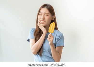Face expression suffering from sensitive teeth and cold, asian young woman, girl feeling hurt, pain eating ice cream, lolly. Toothache molar tooth at home, dental problem isolated on white background.