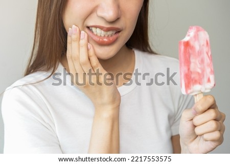 Face expression suffering from sensitive teeth and cold, asian young woman, girl hand touching her cheek, feeling hurt, pain eating ice cream, lolly. Toothache molar tooth at home, dental problem.
