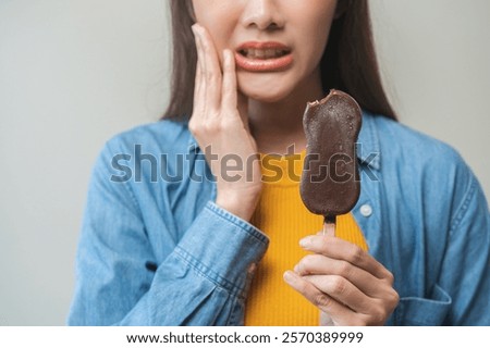 Face expression suffering from sensitive teeth and cold, asian young woman touching cheek, hurt or pain eating ice cream with chocolate. Toothache molar tooth, dental problem isolated on background.