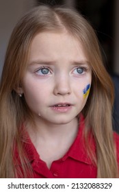 The Face Of A Frightened Girl, A Child Crying, Tears Flowing, Painted On Her Cheek In The Yellow-blue Colors Of The Ukrainian Flag, A Request For Help. Children Ask For Peace