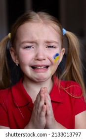 the face of a frightened girl, a child crying, tears flowing, painted on her cheek in the yellow-blue colors of the Ukrainian flag, a request for help. Children ask for peace