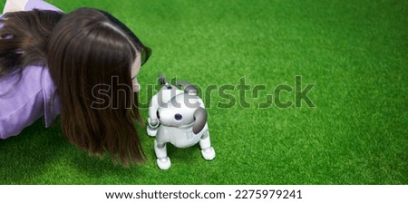 The face of a girl interacting with her pet robot dog on the green lawn. Copy space.                               