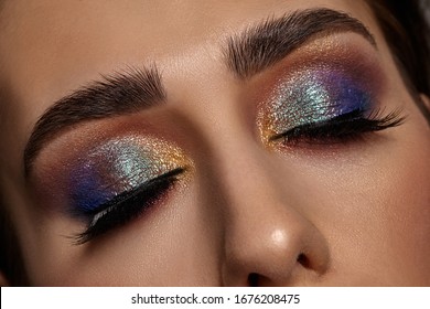 Face Of A Girl With Luxury Makeup And Perfect Skin. She Has Closed Her Eyes. Blue And Golden Eyeshadow, False Eyelashes And Brown Eyebrows. Close Up