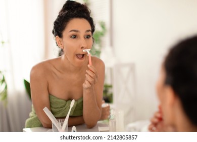 Face hair depilation. Lovely millennial woman in towel shaving upper lip with razor near mirror at home, empty space. Beautiful young female making domestic depilation at bathroom