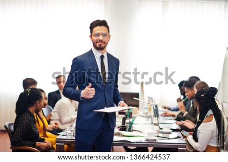 Face of handsome arabian business man, holding clipboard and show thumb up on the background of business peoples multiracial team meeting, sitting in office table. 