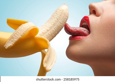 A face of a hot girl that is licking a half-peeled yellow banana.