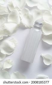 Face Lotion Bottle And Rose Petal On White Background. Flat Lay, Top View