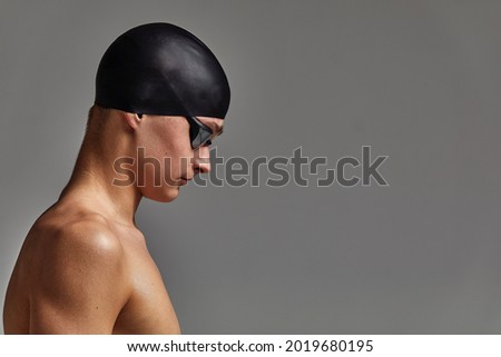Face of a man swimmer close-up, gray background, copy space, young guy swimmer in a mask and swimming cap