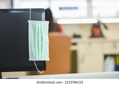 Face Mask Hanging On The Computer Screen In An Empty Office