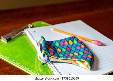 Face Mask Resting On Top Of Back To School Supplies Of Paper, Pencil And A Clip Board