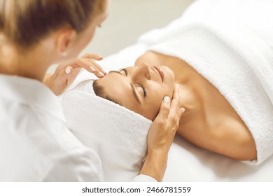 Face massage. Beautiful woman with closed eyes relaxes in spa center during facial massage. Masseuse massages face of client of beauty salon. Concept of skin care, spa, treatment and facial massage.  - Powered by Shutterstock