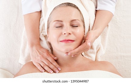 Face massage in spa environment macro. Attractive woman with close eyes taking skin care. Massage face selective focus.