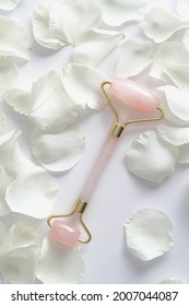 Face massage tool roller with rose petals on white background. Flat lay, top view.