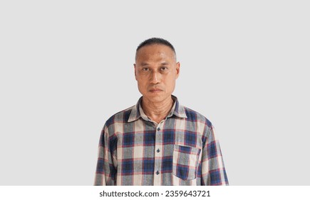 The face of a middle-aged Asian man wearing a plaid shirt looking at the camera with an angry expression isolated on a gray background. The concept of inner anger - Powered by Shutterstock