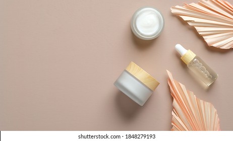 Face Moisturizer Cream, Serum, Essential Oil In Glass Bottle And Dry Flowers On Beige Background. Flat Lay, Top View. Set For Skin And Body Care Beauty Products.