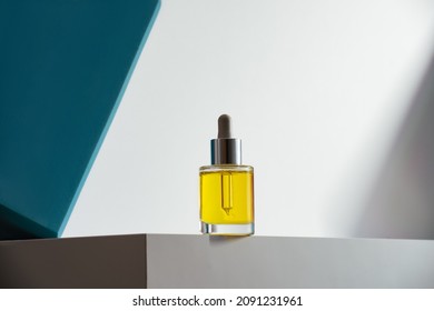 face oil in glass bottle with dropper on white podium and geometric teal background. Modern self-care minimalism in cosmetics and skin-care. Hero shot