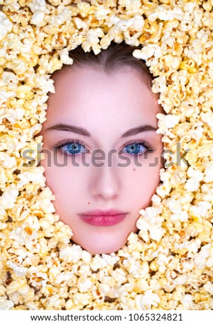 The face in popcorn. Portrait of a young beautiful girl on a background of golden popcorn