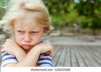 Face portrait of annoyed and unhappy caucasian kid with crossed arms. Upset and angry child concept for family relations, social problems issues and juvenile psychology.  Copy space outdoor background - Powered by Shutterstock