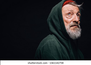 Face portrait of gloomy experienced grey-haired old-aged man with skin lined with wrinkles, dressed in warm shabby clothing as a tramp, looking seriously at camera with hopeless humble expression.