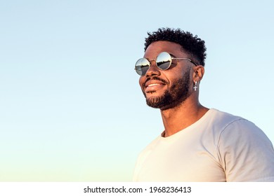 Face Portrait Of A Handsome Black And Young American Man Wearing Sunglasses And Smiling During Sunset At The Beach