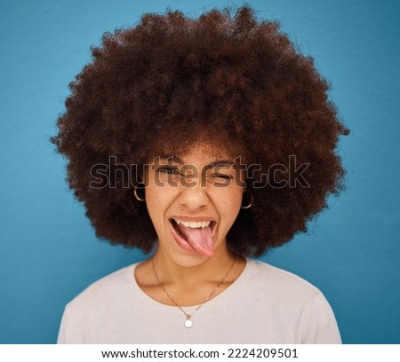 Face, portrait and woman with tongue out being silly and goofy on a blue studio background. Amusing, comic and african american female making a funny, humour face on a backdrop